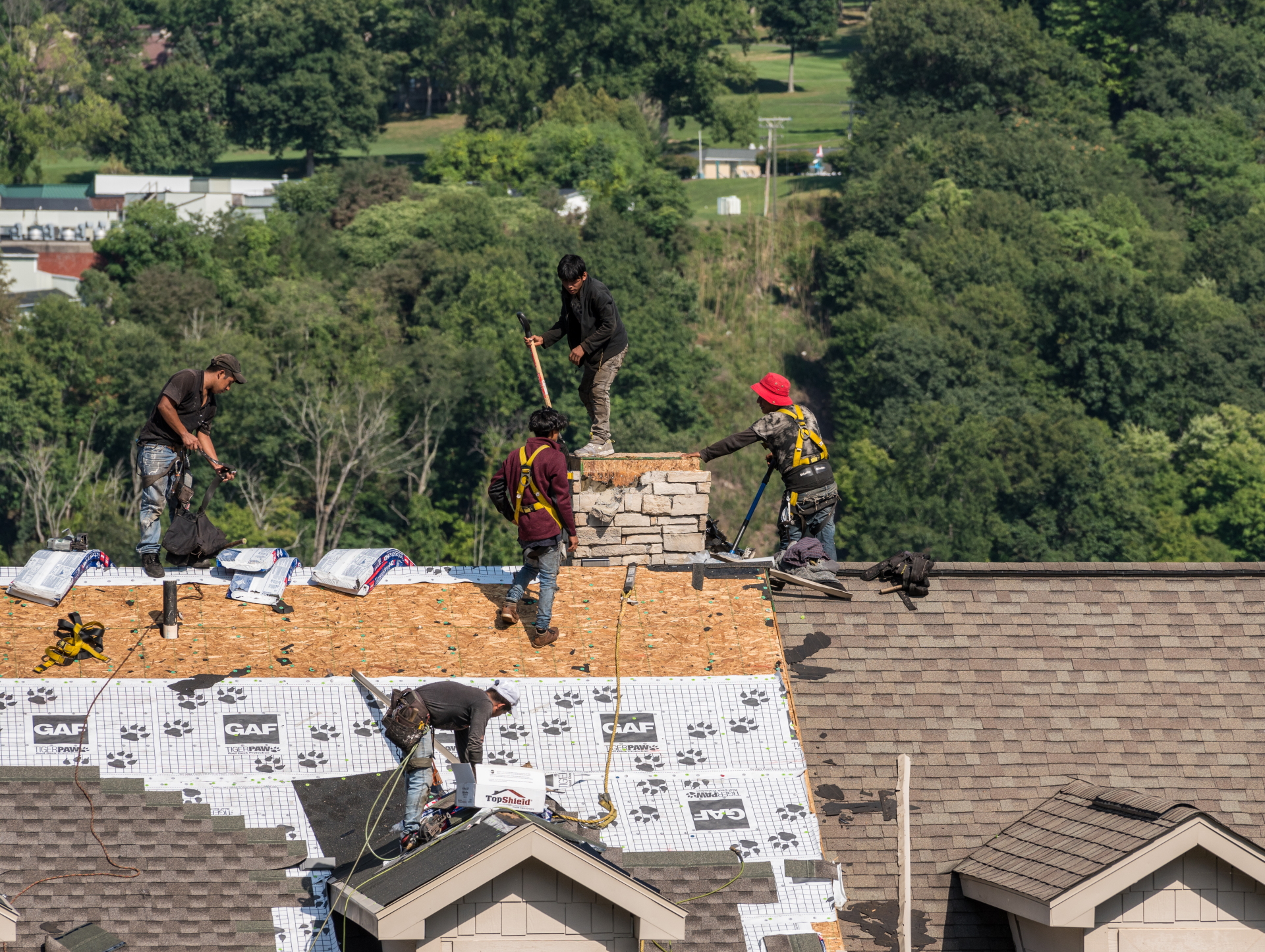 Xterior PRO crew of five installing GAF underlayment and shingles on a residential roof near a stone chimney
