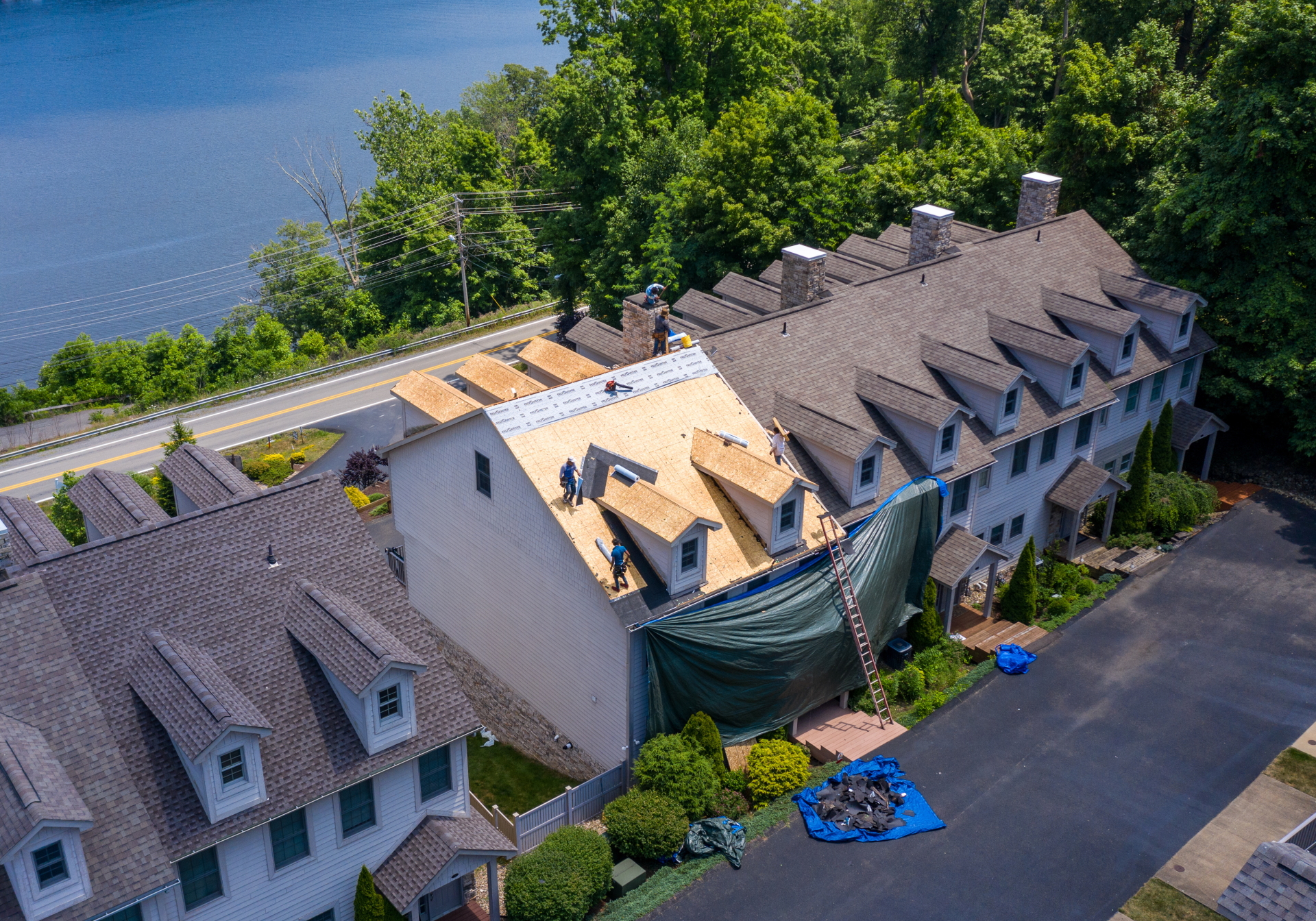 Aerial view of the Xterior PRO crew replacing shingles on a roof, with exposed plywood decking and protective tarps visible