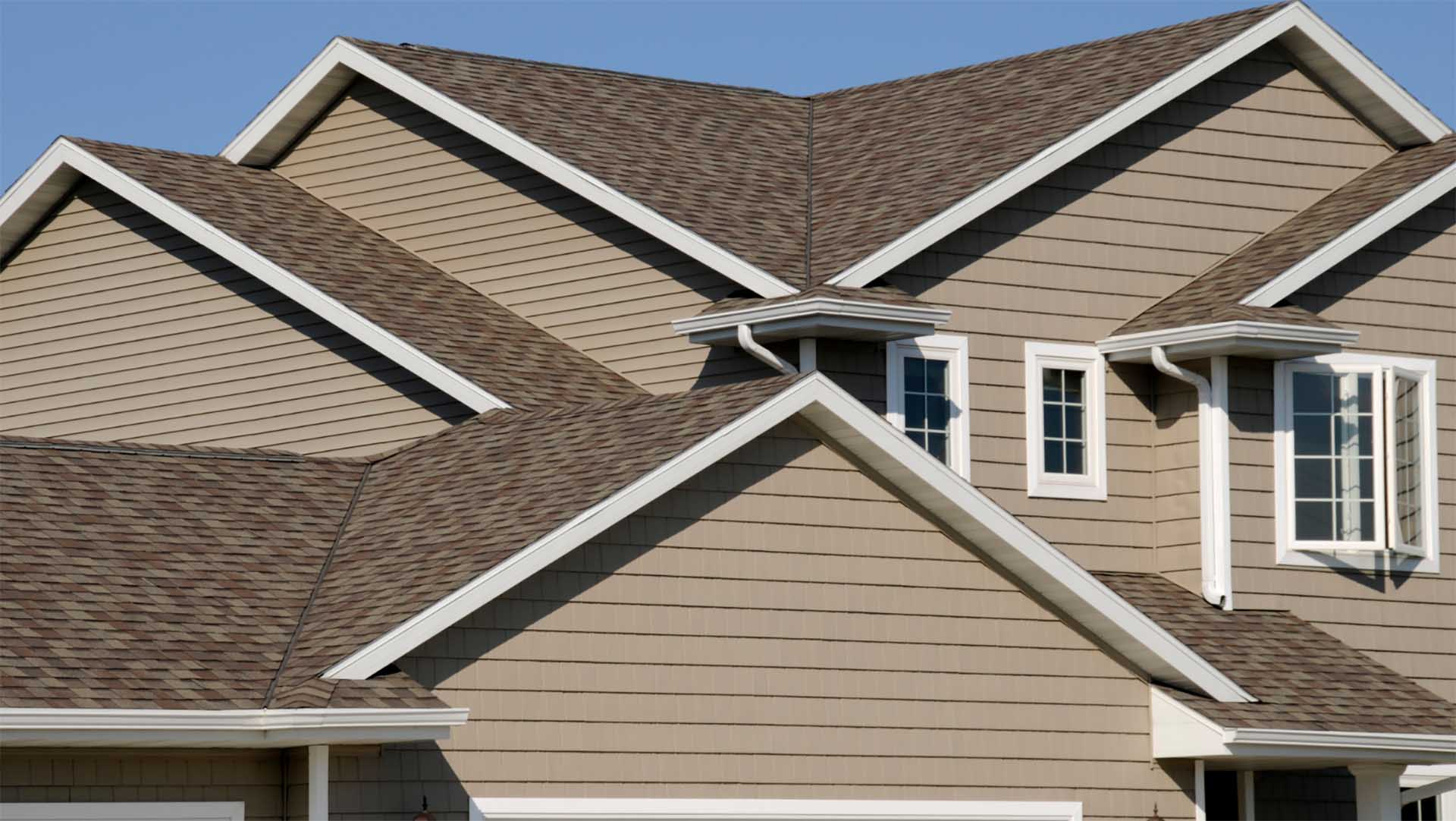 Close-up of gabled rooflines with brown asphalt shingles, white trim and fascia on a two-story home