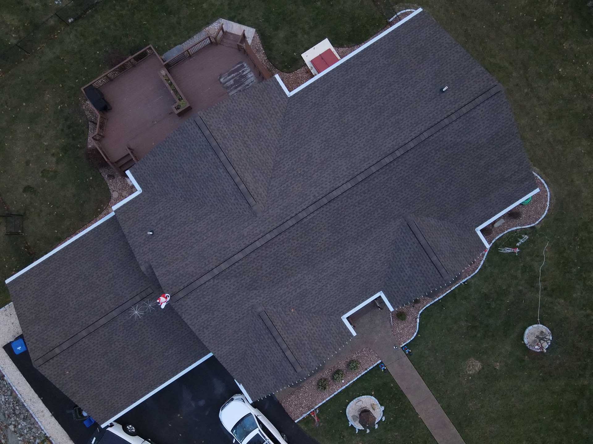 Overhead drone view of a finished gray asphalt shingle roof with new white gutters on a Hudson Valley home