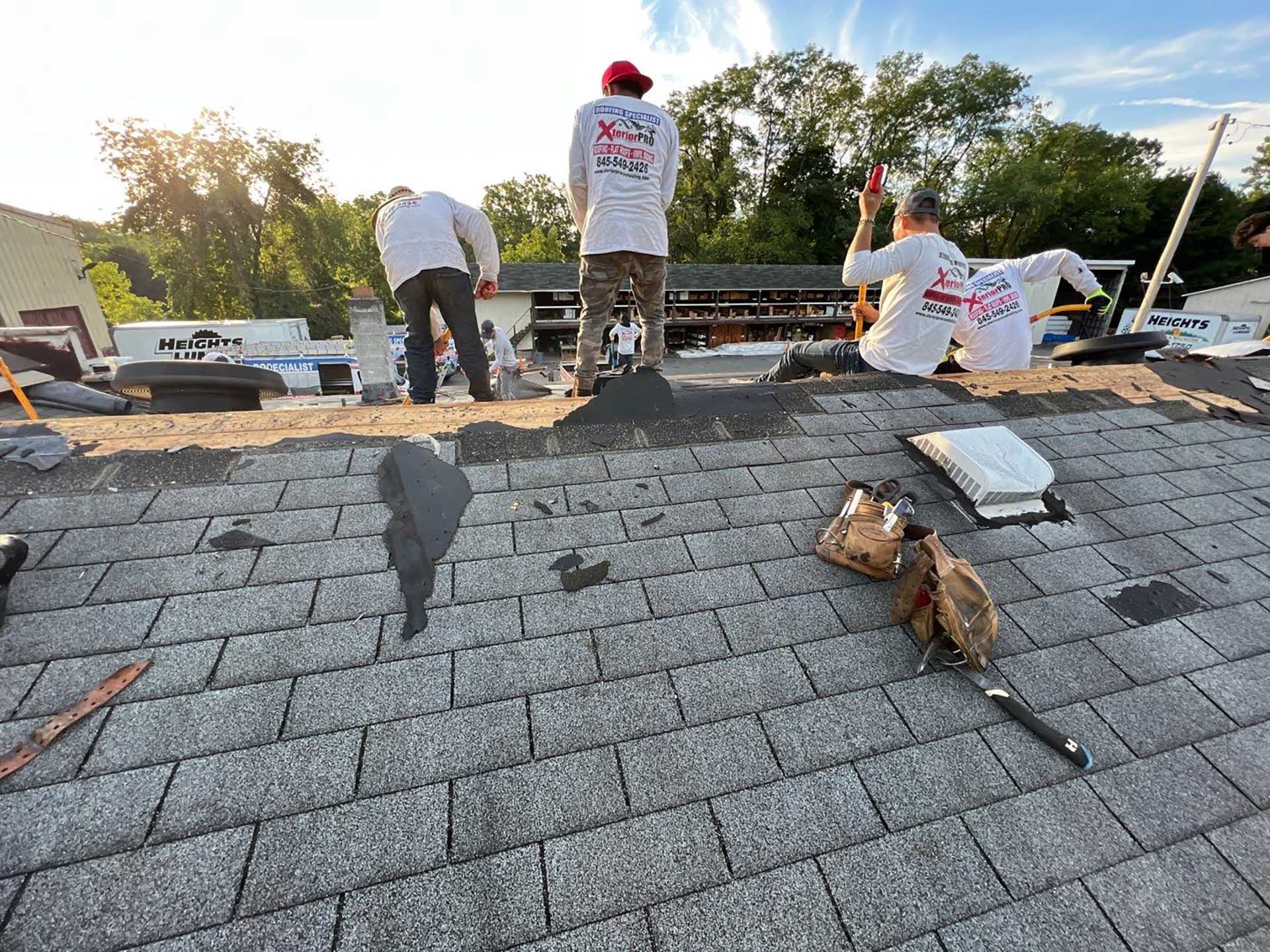 Xterior PRO roofing crew working on a residential shingle roof at sunset