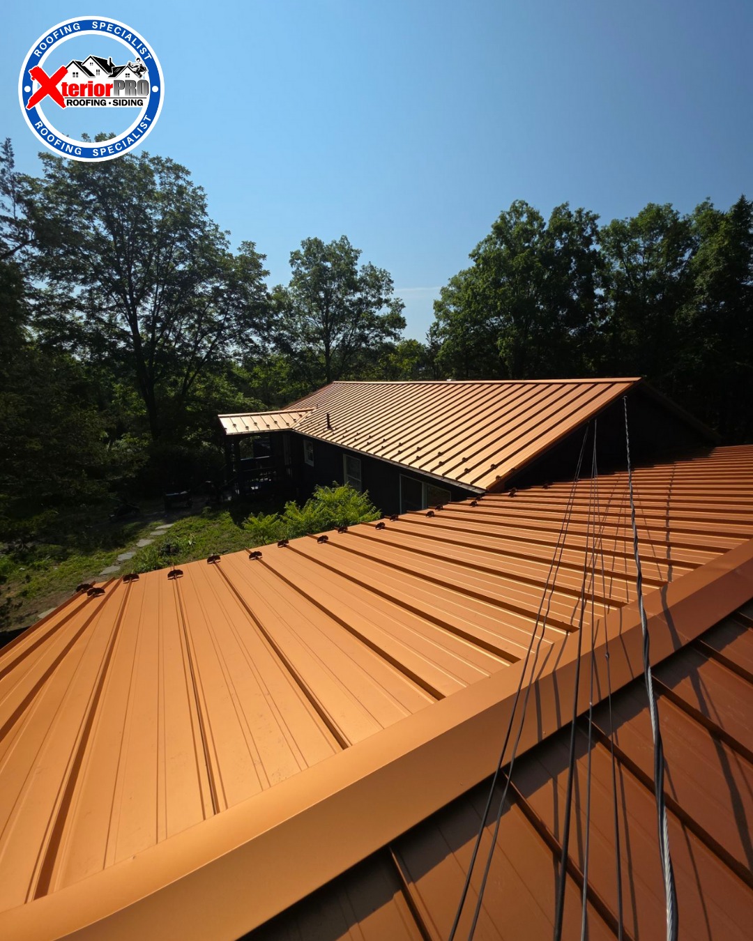 Close-up rooftop view of a completed copper standing seam metal roof installation with snow guards and ridge detail
